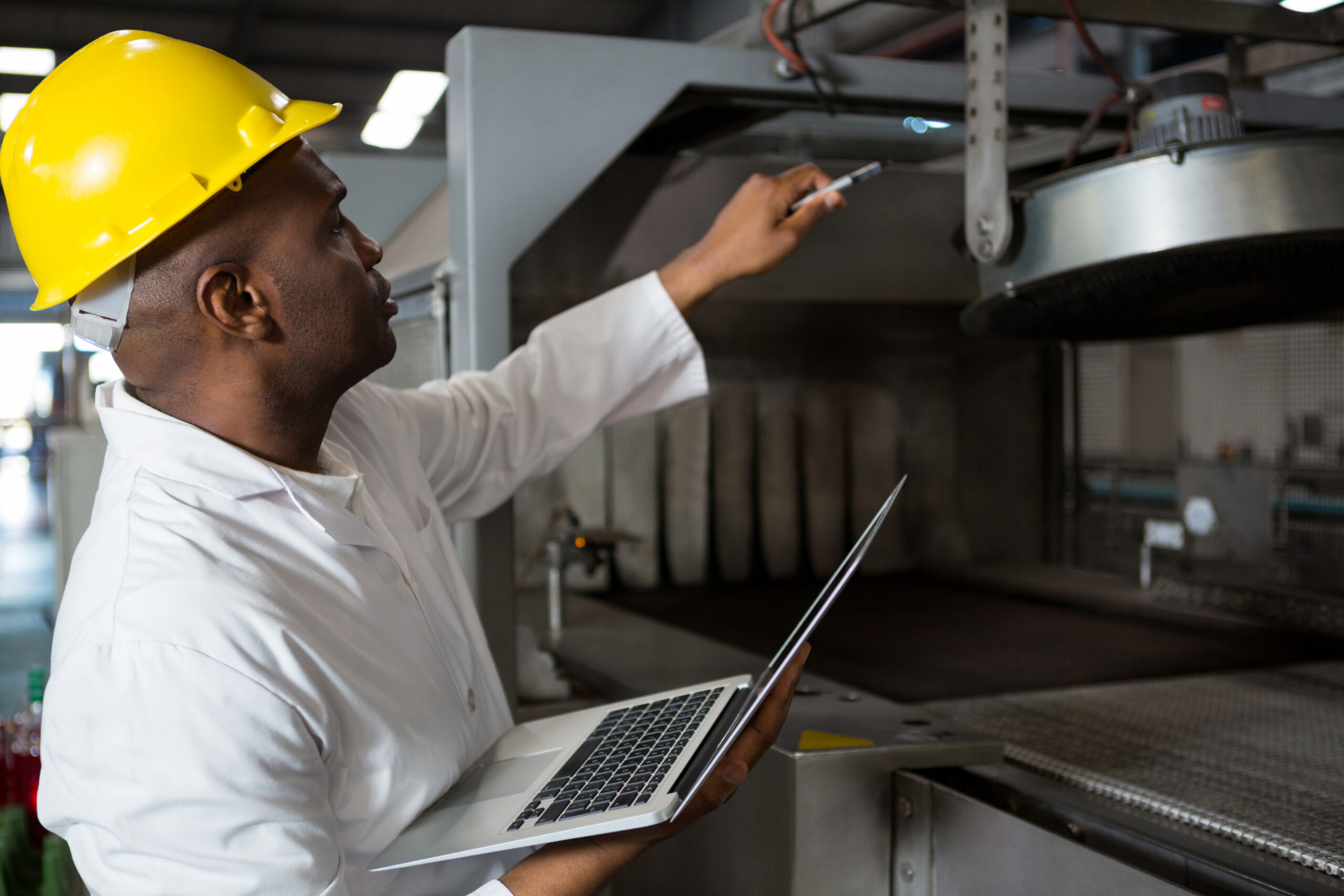 Male worker wearing lab coat while using laptop in juice factory